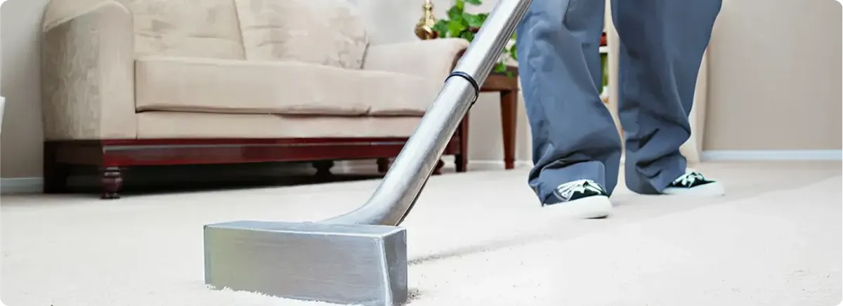 Carpet cleaning technician using a hot-water extraction wand on a light-colored carpet in a living room, {city}, {state}.